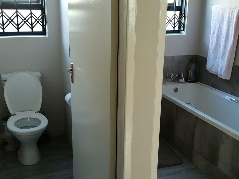 A functional bathroom featuring a separate toilet area and a bathtub with tiled splashback, finished with security bars on the windows.
