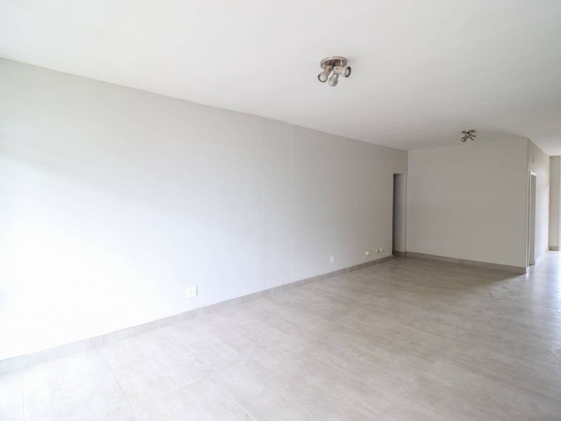 A bright, spacious, and empty living area featuring neutral tiled flooring and modern ceiling spotlights, offering a clean canvas for interior design.