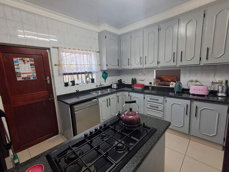 A functional kitchen featuring grey built-in cabinetry, granite countertops, a central island with a gas hob, and tiled backsplash.