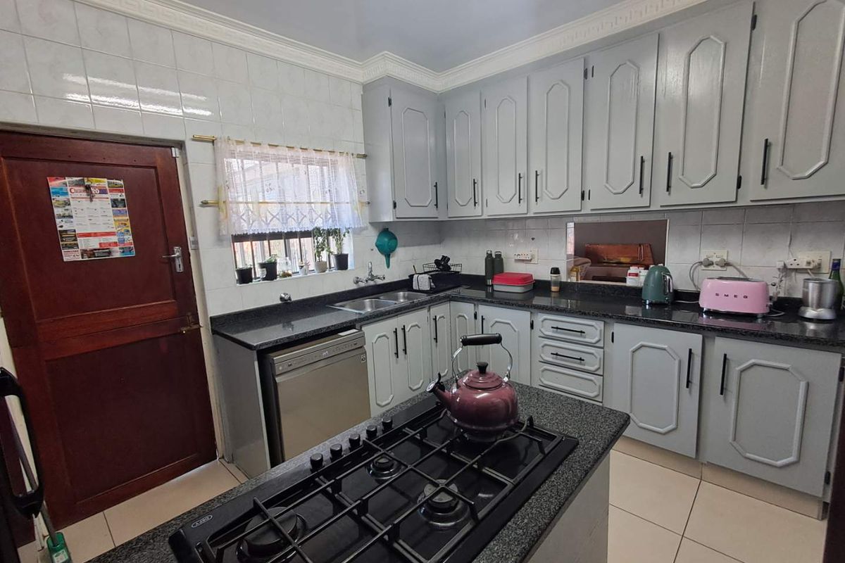 A functional kitchen featuring grey built-in cabinetry, granite countertops, a central island with a gas hob, and tiled backsplash.
