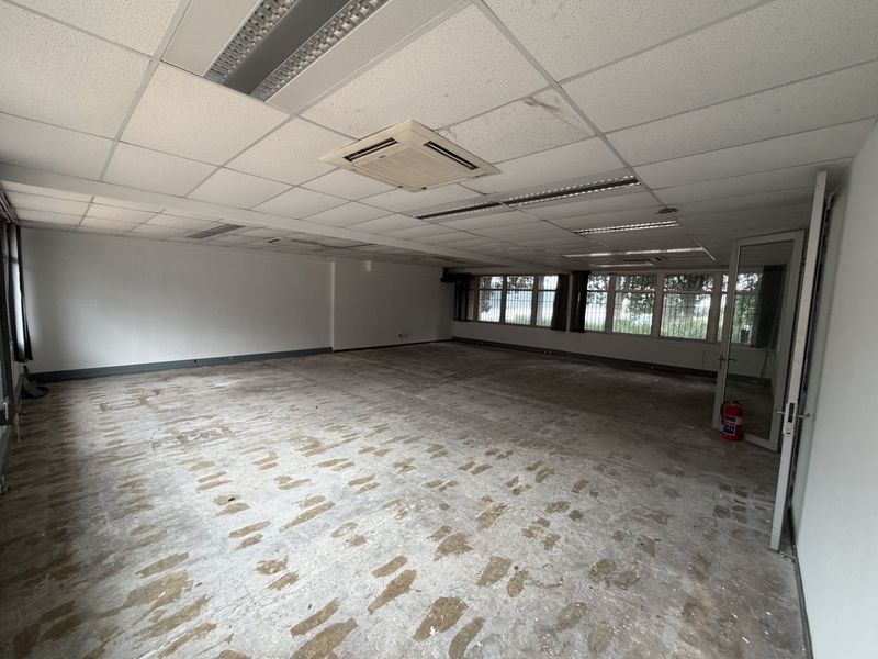 Spacious open-plan office area featuring a suspended ceiling with integrated lighting, cassette air conditioning, and large windows with security bars.