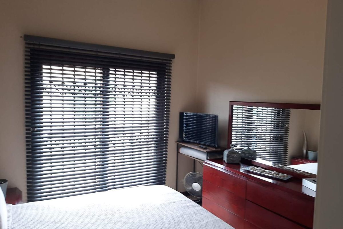 A bedroom featuring a large sliding window with dark horizontal blinds, providing natural light and a neutral wall finish.