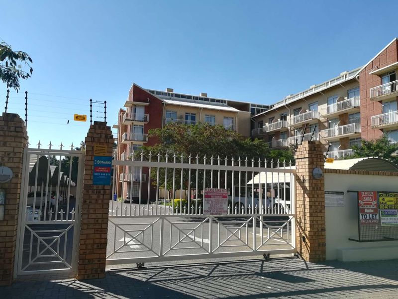 Front entrance view of a multi-story apartment complex featuring secure gated access, brick pillars, electric fencing, and paved driveway.