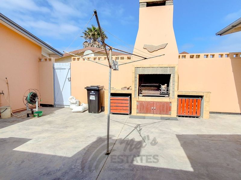 Outdoor patio area featuring a built-in braai, concrete flooring, and enclosed by boundary walls, providing a functional space for outdoor entertaining.