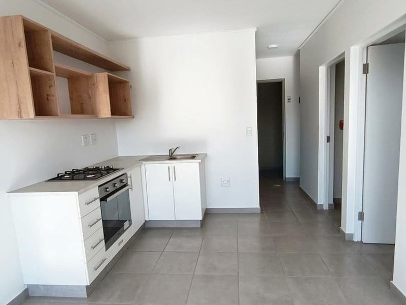 Modern kitchen featuring white cabinetry, gas hob, built-in oven, and open shelving, set against neutral tiled flooring in an open-plan layout.