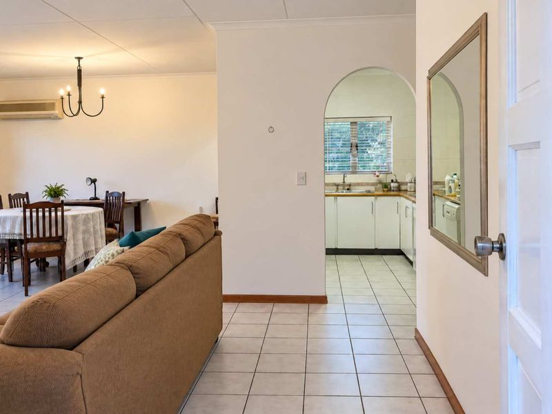 Open-plan living and dining area featuring tiled flooring, an arched entryway to the kitchen, and a wall-mounted air conditioning unit.