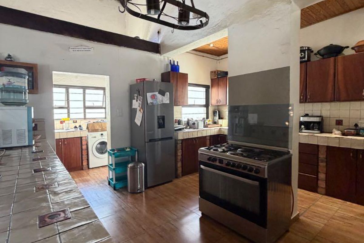 Spacious kitchen featuring a unique exposed thatch ceiling, tiled countertops, wooden cabinetry, and a freestanding gas stove with an extractor hood.