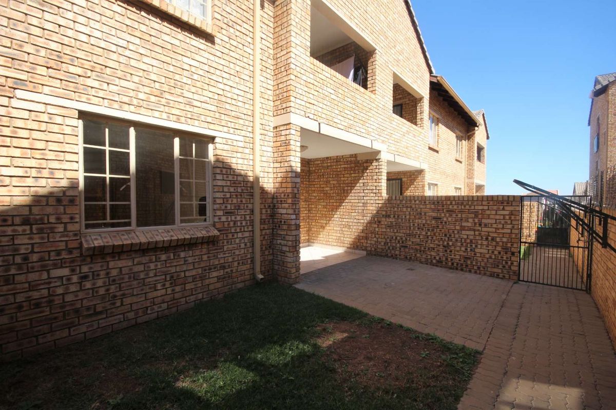 Rear view of the apartment building featuring a face brick facade, a paved patio area, and a small private garden space.