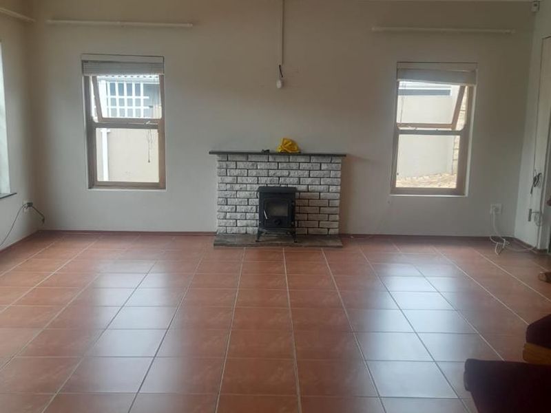 Spacious living room featuring tiled flooring, a central ceiling fan, and a classic brick fireplace with a built-in wood burning stove.