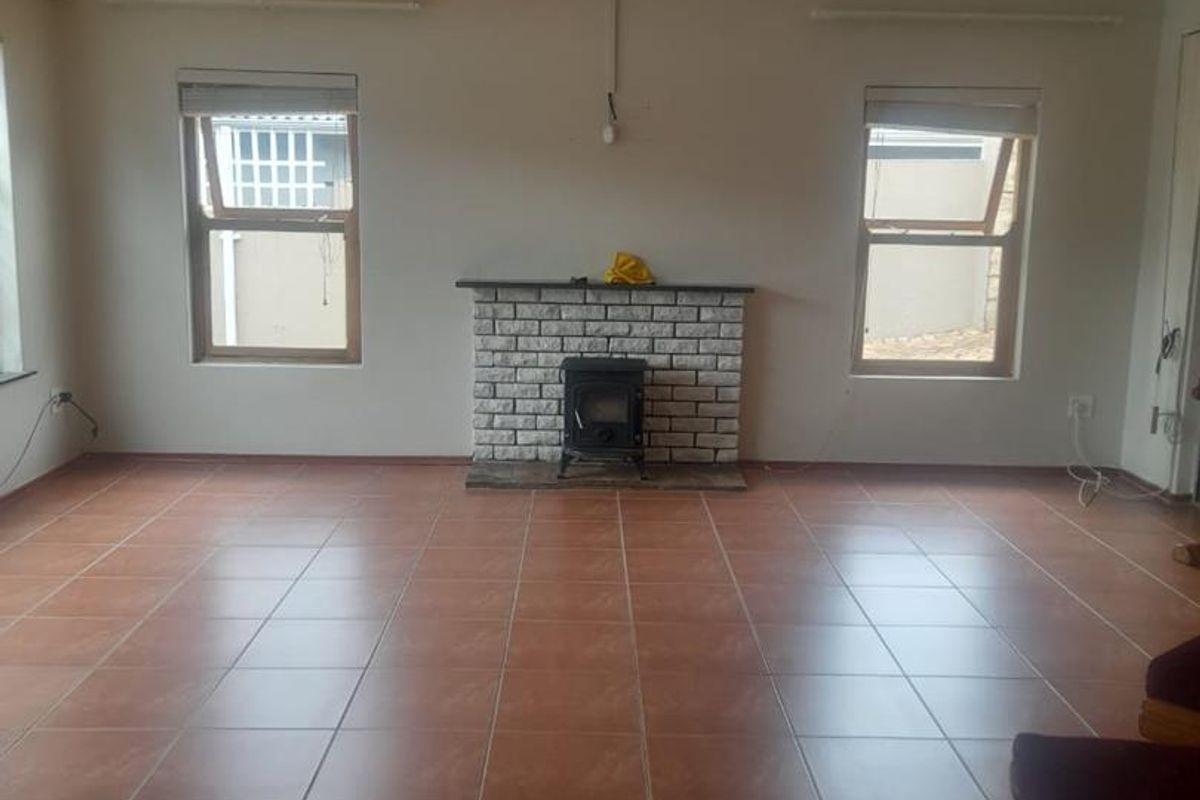 Spacious living room featuring tiled flooring, a central ceiling fan, and a classic brick fireplace with a built-in wood burning stove.