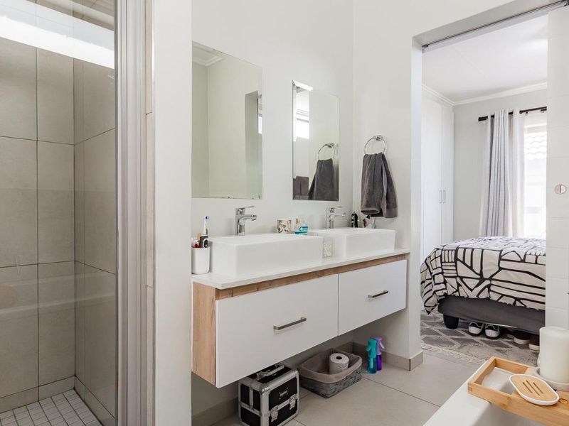Modern en-suite bathroom featuring a double vanity with vessel sinks, sleek chrome fixtures, and a spacious walk-in shower with neutral tiling.