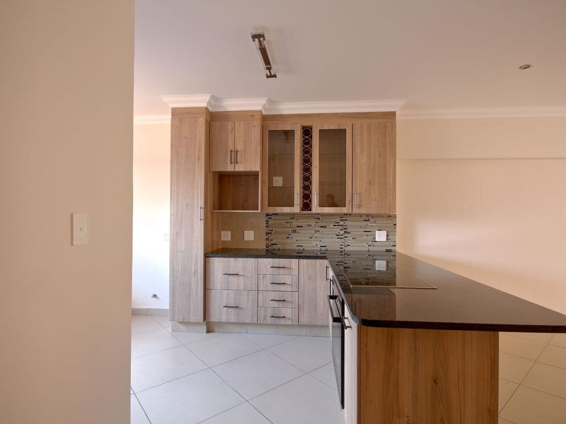 Modern kitchen featuring light wood-grain cabinetry, dark granite countertops, a mosaic tile backsplash, and integrated appliances in an open-plan layout.