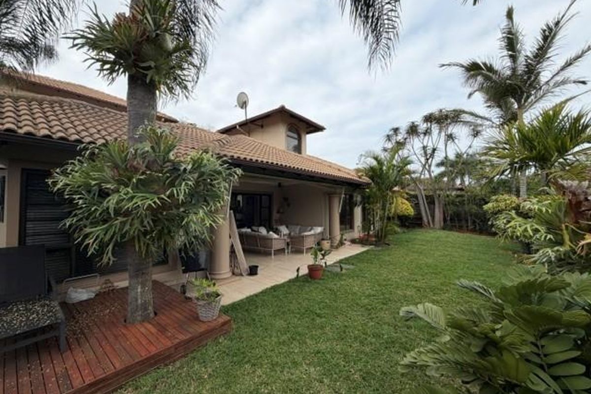 Rear view of the townhouse featuring a covered patio, wooden decking, and a well-maintained garden area.