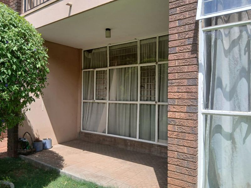 A covered patio area featuring tiled flooring and large glass window panels with security bars, providing access to the interior living space.