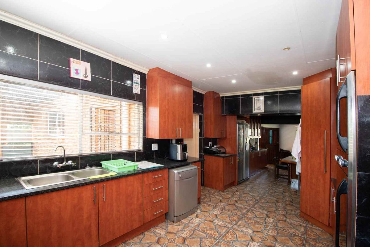 A functional kitchen featuring wood-finish cabinetry, dark tiled splashbacks, a double basin sink, and tiled flooring, offering ample storage and workspace.