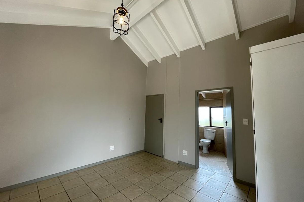 Spacious bedroom featuring vaulted ceilings with exposed rafters, tiled flooring, and direct access to an en-suite bathroom.