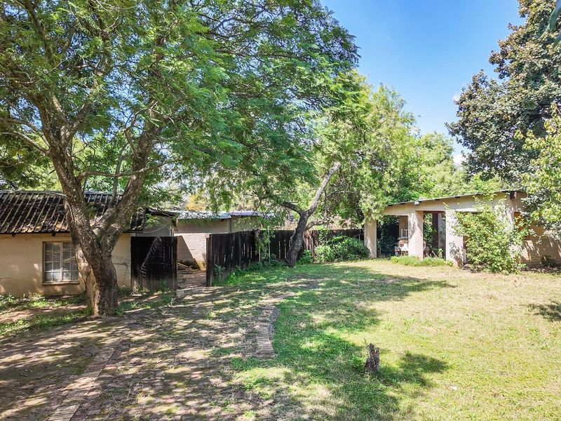 Spacious rear garden area featuring mature trees, a paved pathway, and access to outbuildings with potential for landscaping or renovation.