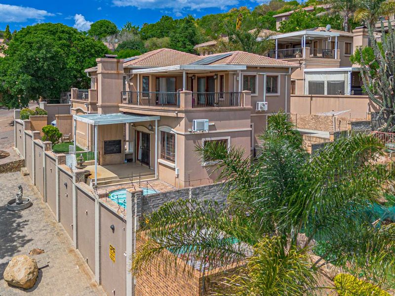 Aerial view of a multi-level residential property featuring a tiled roof, balcony with wrought iron railings, and a paved driveway within a secure estate.