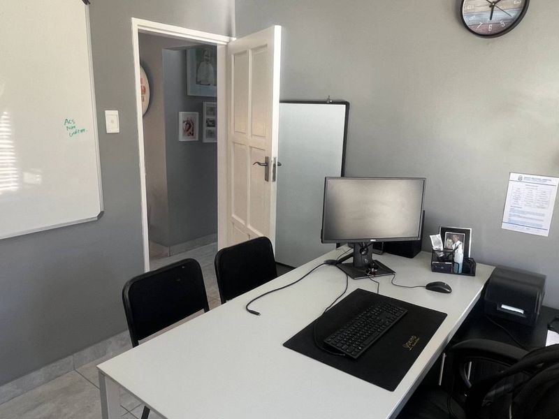A functional home office space featuring neutral grey walls, tiled flooring, and a standard internal door leading to an adjacent room.