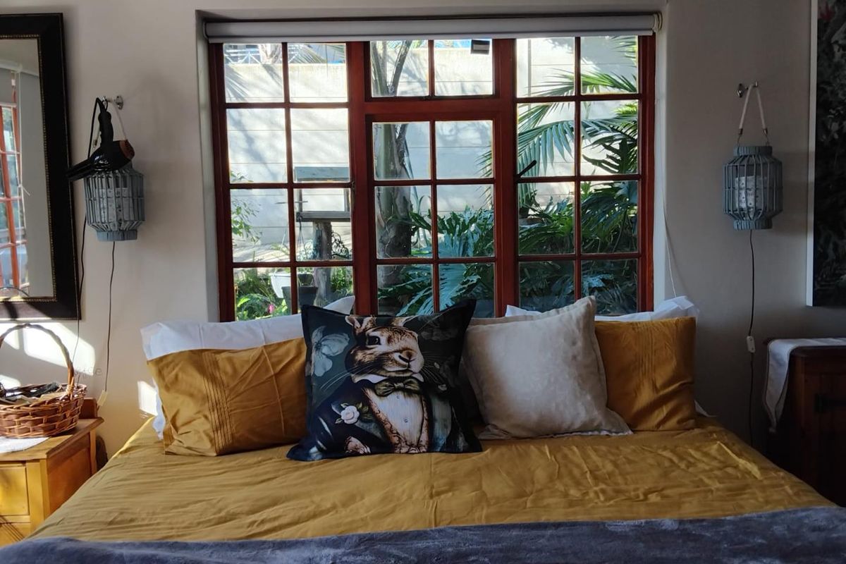 A cozy bedroom featuring a large timber-framed window overlooking a lush garden, providing natural light and a pleasant outdoor view.