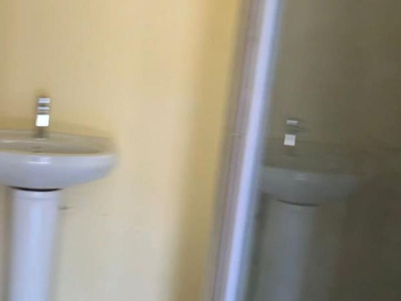 A functional bathroom featuring a pedestal basin and a glass-enclosed shower, finished with neutral wall paint and tiled flooring.