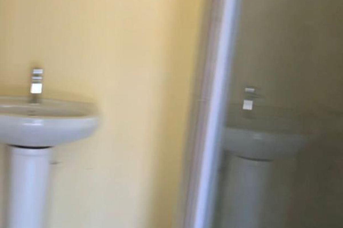 A functional bathroom featuring a pedestal basin and a glass-enclosed shower, finished with neutral wall paint and tiled flooring.