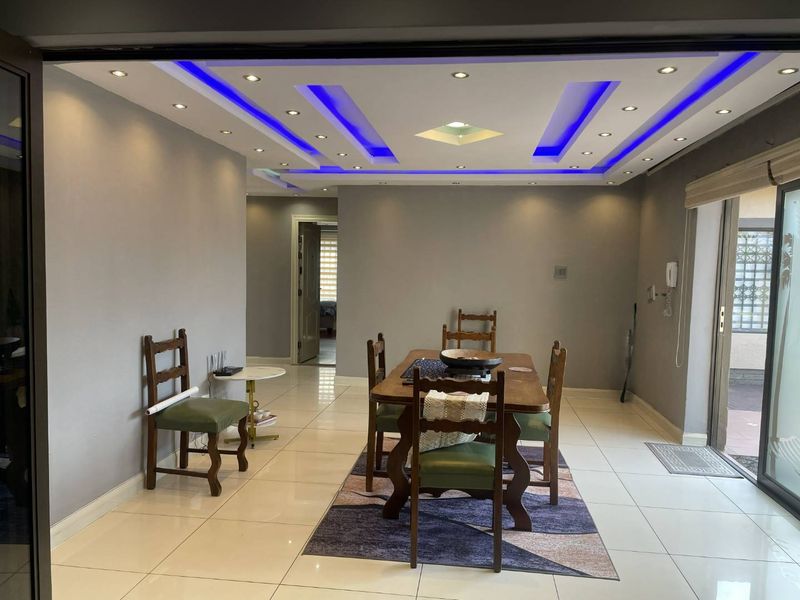 Dining area featuring modern recessed ceiling lighting with blue LED accents and large format floor tiles, leading to an outdoor patio area.