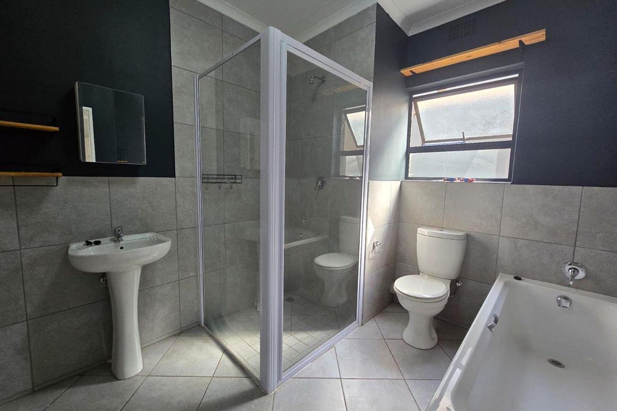 Modern bathroom featuring a glass-enclosed shower, pedestal basin, toilet, and a separate bathtub with neutral wall and floor tiling.
