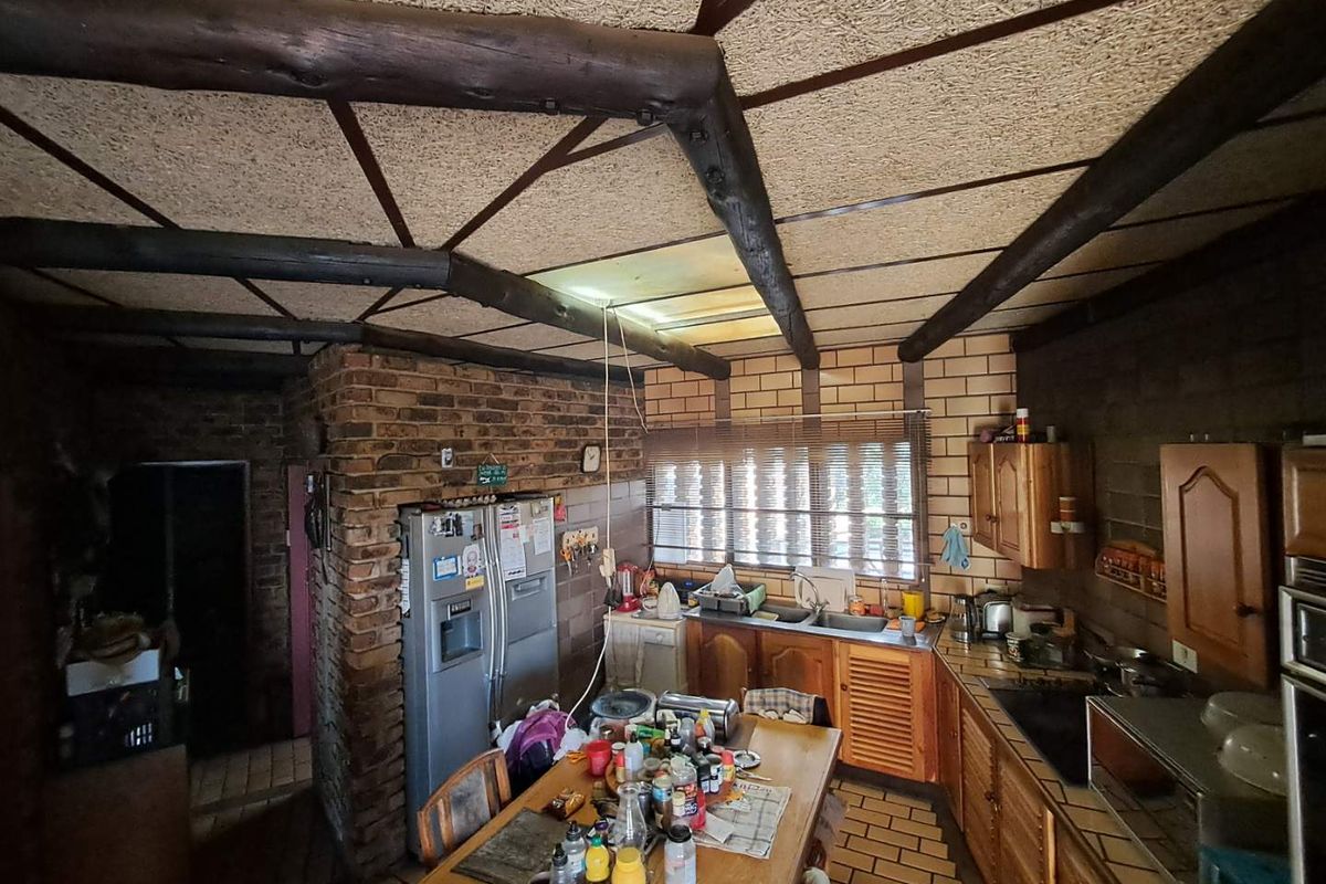 A rustic kitchen featuring exposed timber beams, brick feature walls, wooden cabinetry, and a built-in oven, offering a traditional aesthetic with potential for modernization.