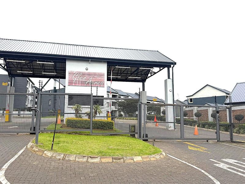The secure entrance gate of Glen Acres apartment complex, featuring a metal security gate, paved driveway, and covered guardhouse structure.