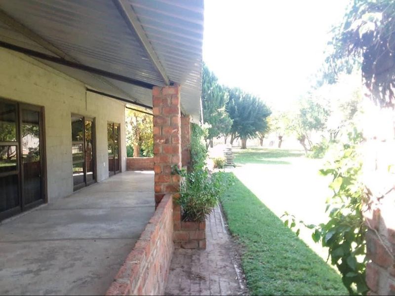 A covered outdoor patio featuring exposed brick pillars and concrete flooring, providing direct access to the garden through sliding glass doors.