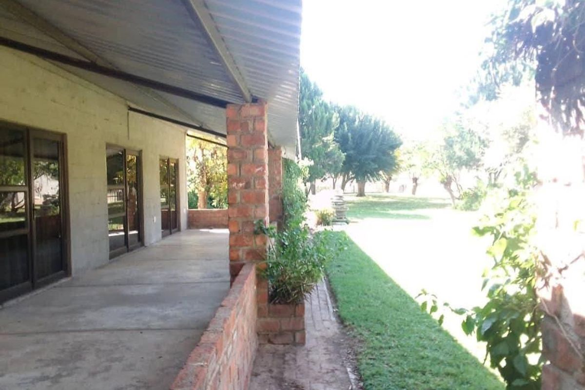 A covered outdoor patio featuring exposed brick pillars and concrete flooring, providing direct access to the garden through sliding glass doors.