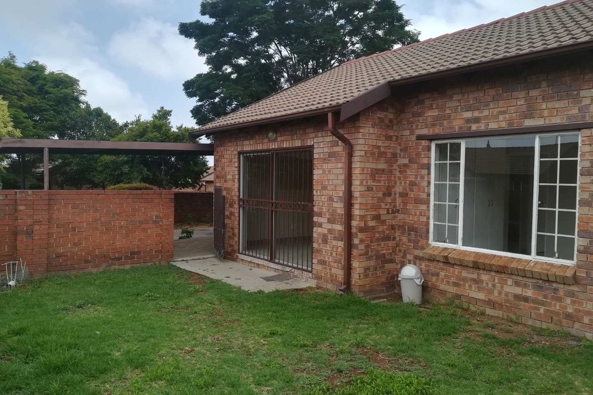 Rear view of a face brick townhouse featuring a small lawn, covered patio area, and secure sliding door access.