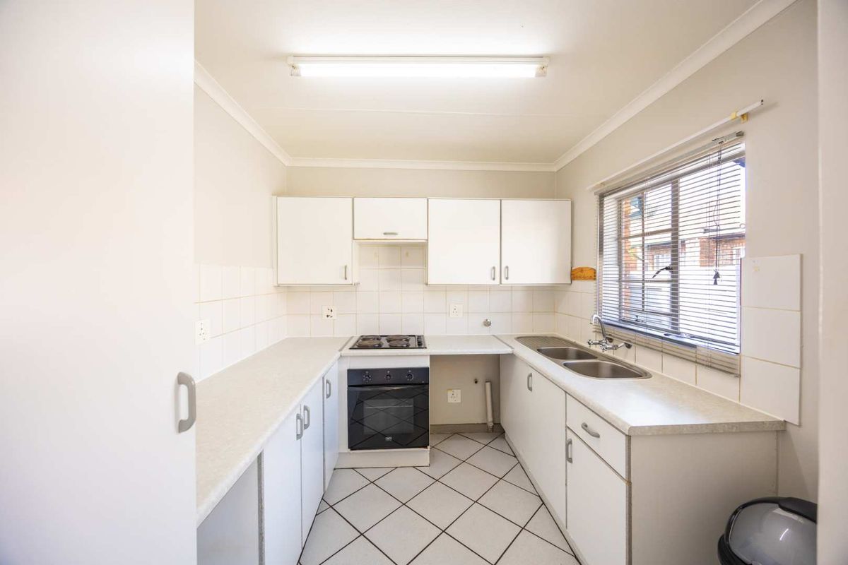 A functional, galley-style kitchen featuring white cabinetry, laminate countertops, a built-in oven with gas hob, and tiled flooring.
