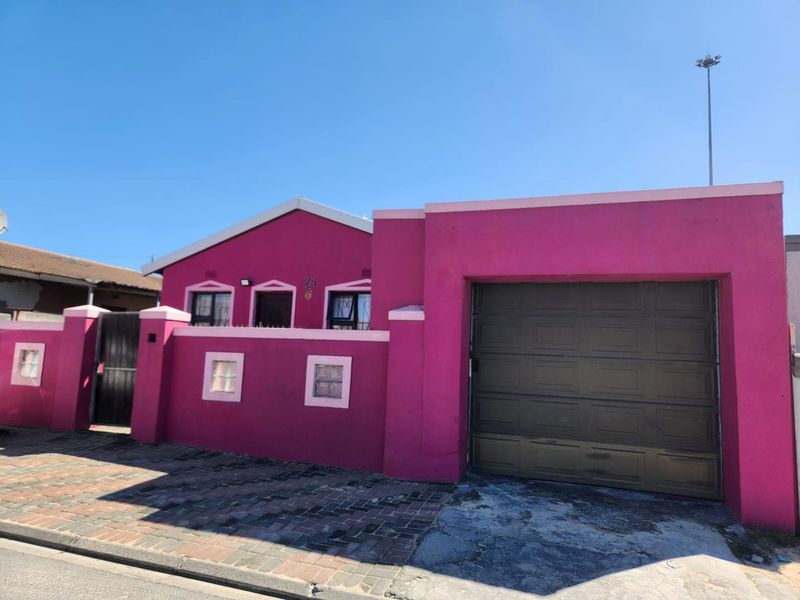 Front exterior view of a house featuring a bright pink facade, a single garage, and a paved driveway with a secure boundary wall.