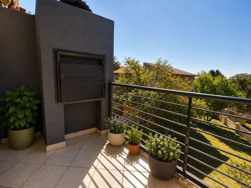 A private balcony featuring a built-in braai, tiled flooring, and a metal balustrade, offering pleasant views of the surrounding greenery.