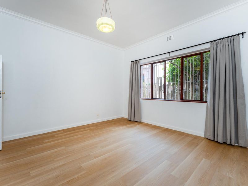 A bright, empty bedroom featuring light-toned laminate flooring, crown molding, and a large window with security bars, offering a clean and neutral living space.