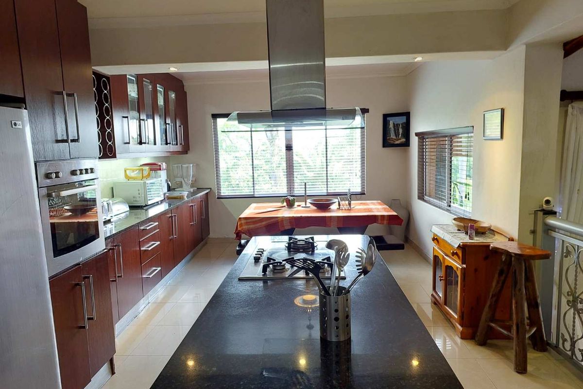 Spacious kitchen featuring dark wood cabinetry, granite countertops, a central island with a built-in gas hob, and a stainless steel extractor fan.