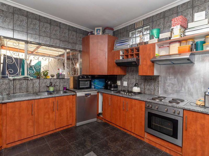 A functional kitchen featuring wood-finish cabinetry, granite-look laminate countertops, built-in oven and hob, and full-height wall tiling.