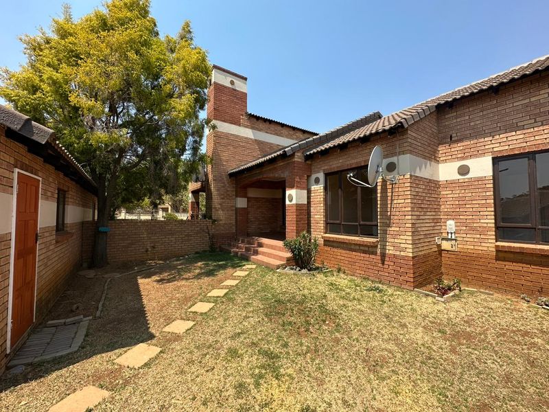 Rear view of a face brick townhouse featuring a small garden, stepped entrance, and tiled roof structure.