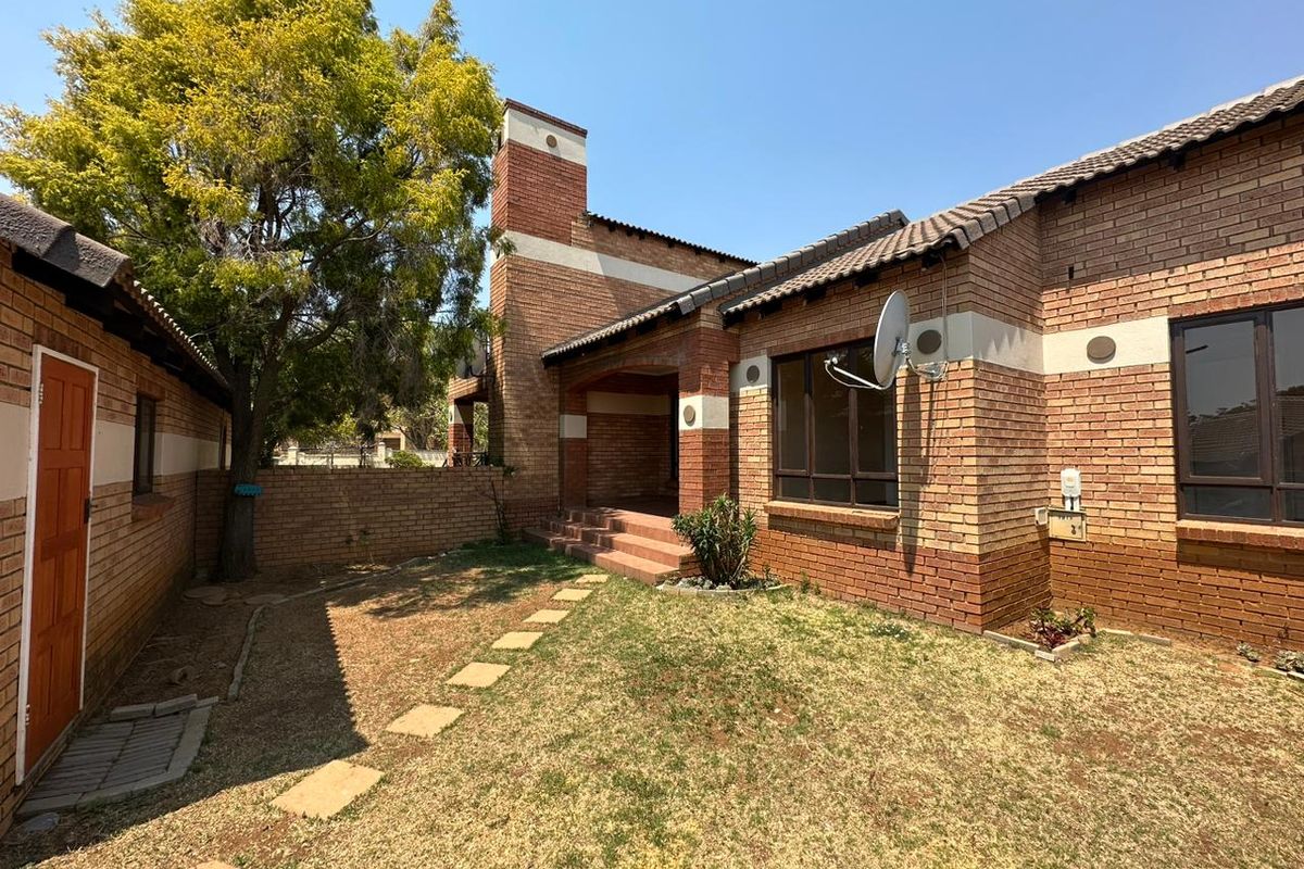 Rear view of a face brick townhouse featuring a small garden, stepped entrance, and tiled roof structure.