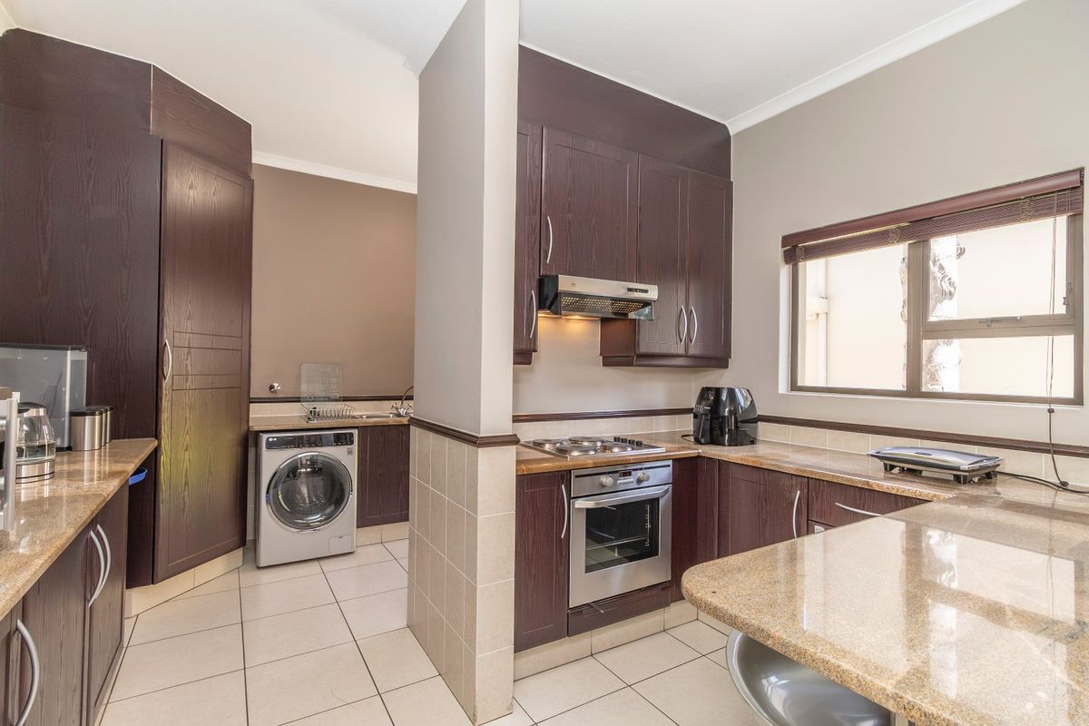Functional kitchen featuring dark wood cabinetry, granite countertops, built-in oven and hob, with an adjoining laundry area and tiled flooring throughout.