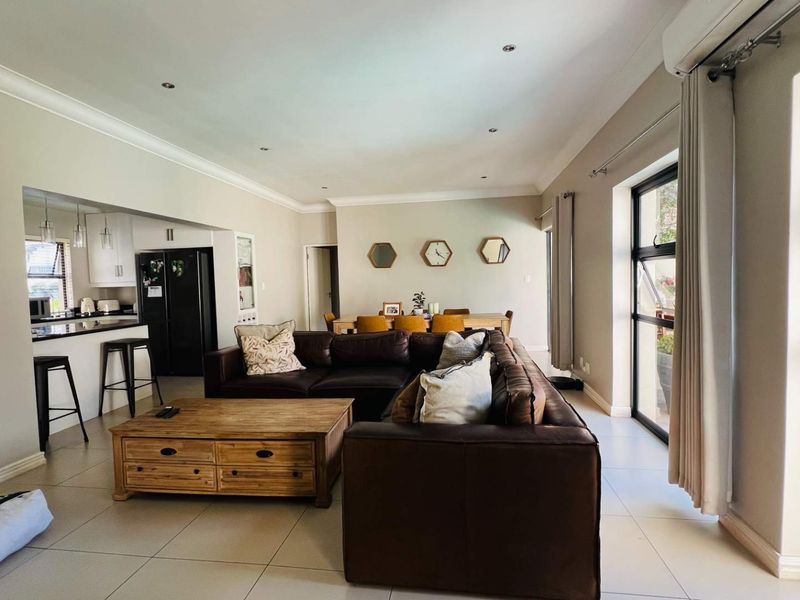 Spacious open-plan living and dining area featuring tiled floors, recessed lighting, and a modern kitchen with a breakfast island and built-in cabinetry.