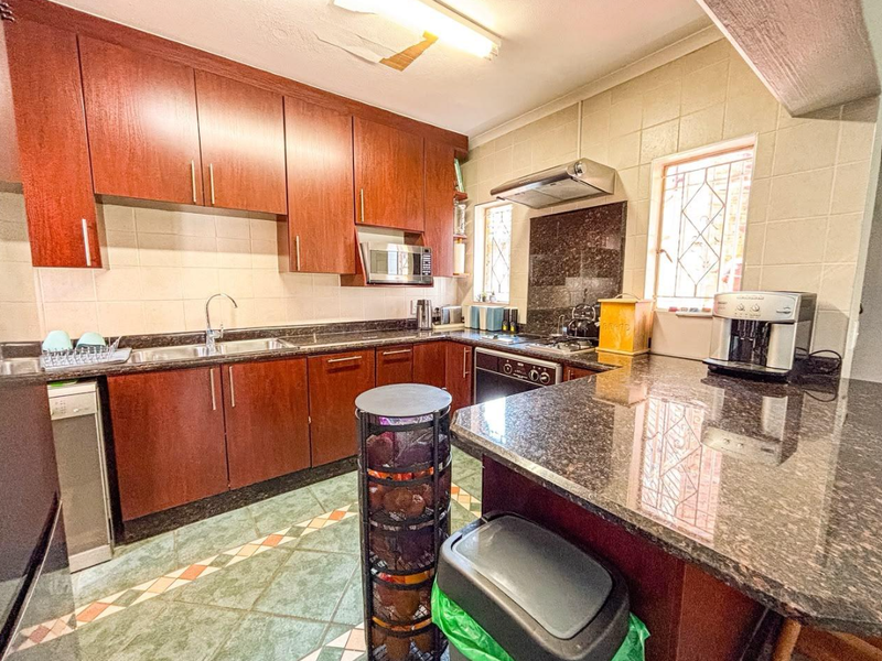 A functional kitchen featuring dark wood cabinetry, granite countertops, built-in appliances, and tiled flooring, with some minor ceiling damage visible.