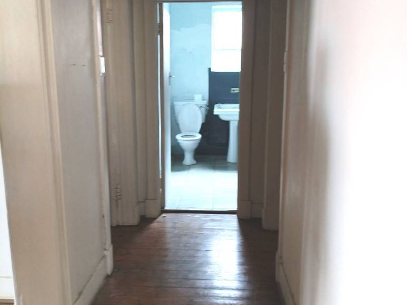 A narrow hallway featuring original timber flooring and traditional architraves, leading towards a bathroom area.
