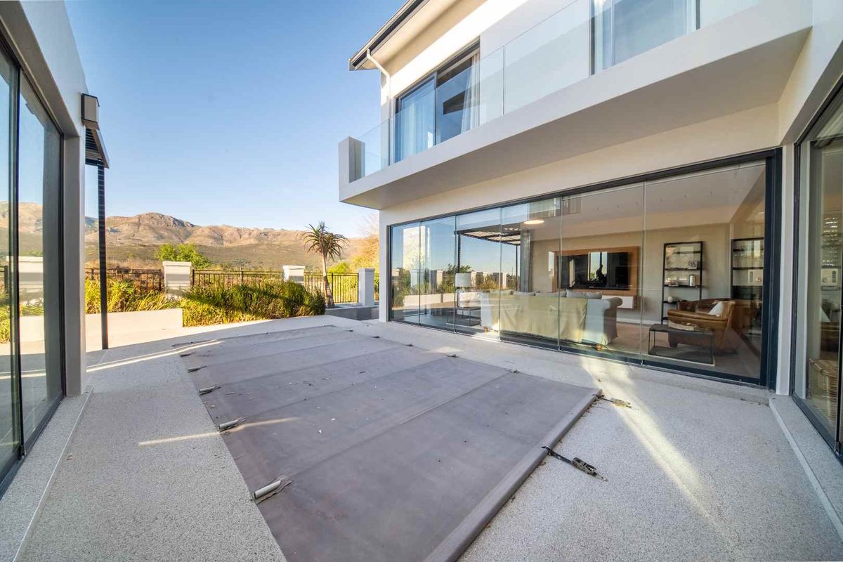 Modern rear exterior featuring a paved patio, pool cover, and large sliding glass doors opening into the living area with mountain views.