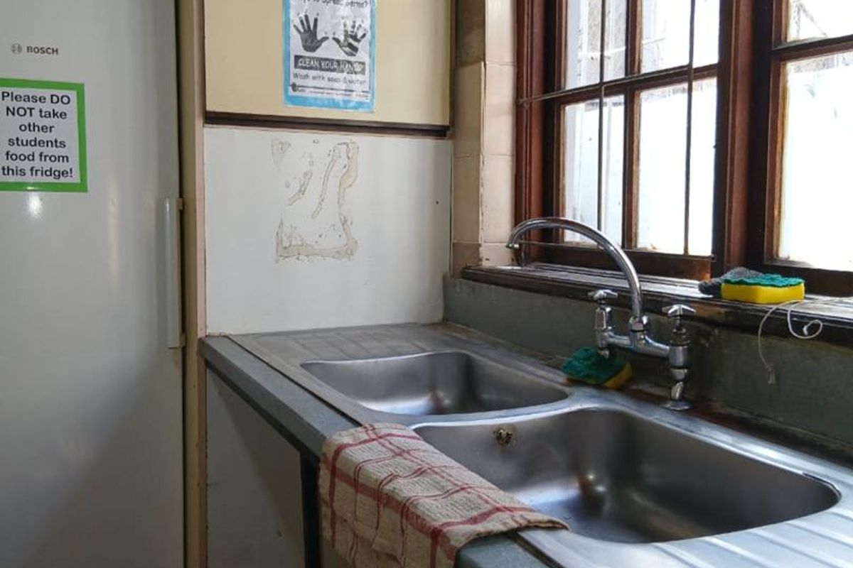 A dated kitchen area featuring a double stainless steel sink, laminate countertop, and timber-framed window, requiring significant cosmetic updates and repairs.