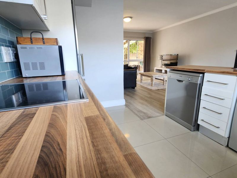 Open-plan kitchen featuring butcher block countertops, subway tile backsplash, and integrated appliances, flowing seamlessly into a bright living area with sliding door access.