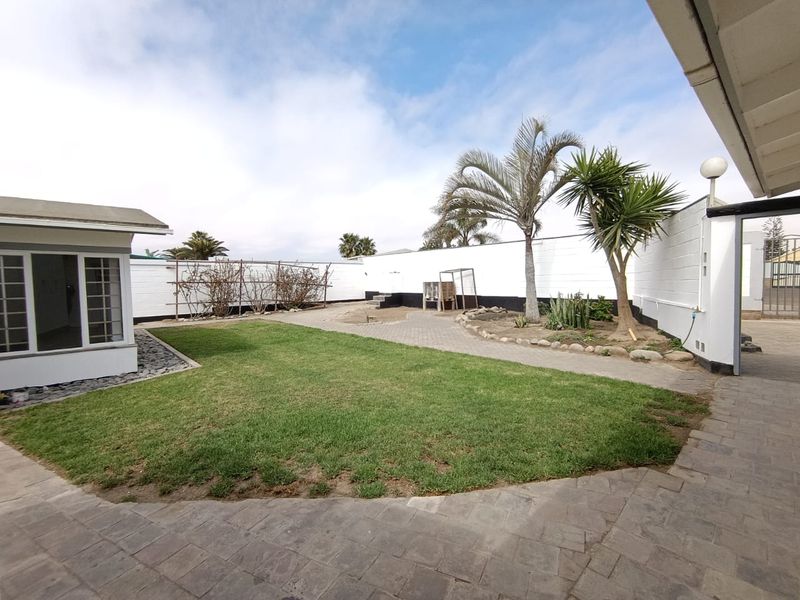 A spacious rear garden featuring a paved patio area, a well-maintained lawn, and secure boundary walls, providing a private outdoor space.