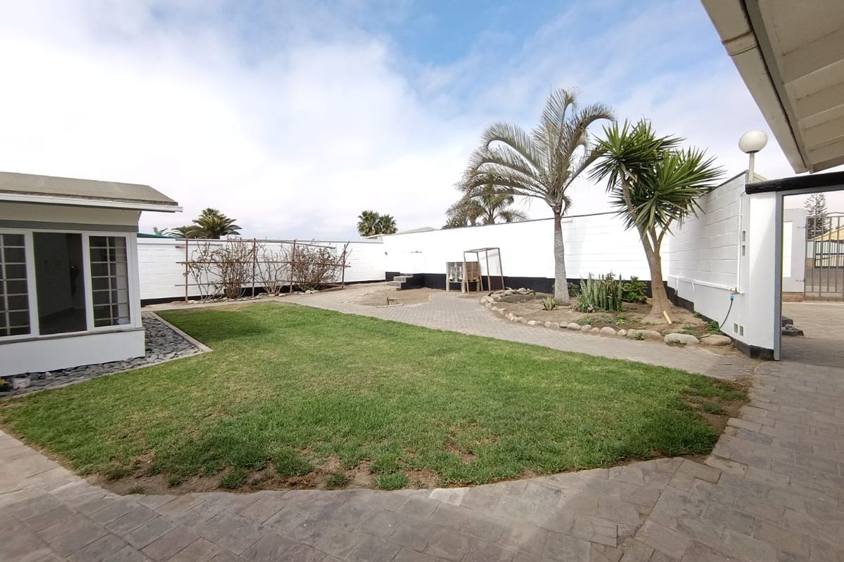 A spacious rear garden featuring a paved patio area, a well-maintained lawn, and secure boundary walls, providing a private outdoor space.